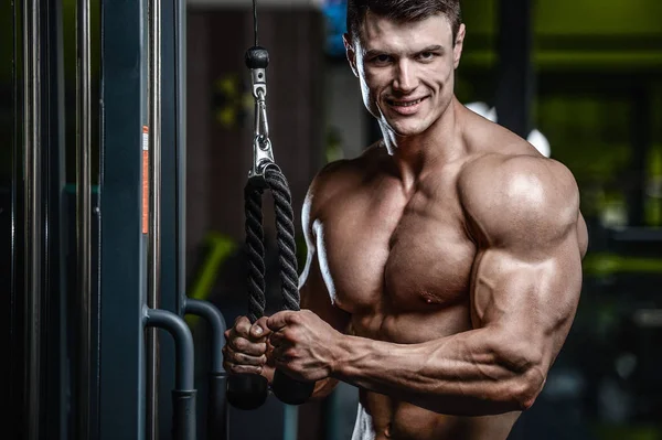 Guapo modelo joven entrenamiento brazos en el gimnasio — Foto de Stock