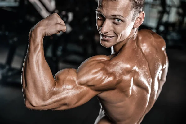 Guapo modelo joven entrenamiento brazos en el gimnasio — Foto de Stock