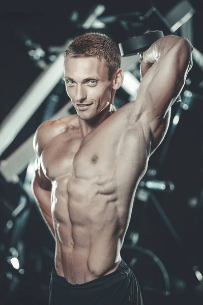 Guapo modelo joven entrenamiento brazos en el gimnasio — Foto de Stock