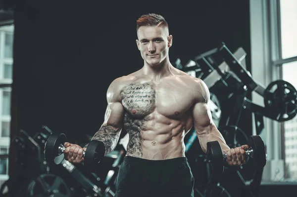 Guapo modelo joven entrenamiento brazos en el gimnasio — Foto de Stock