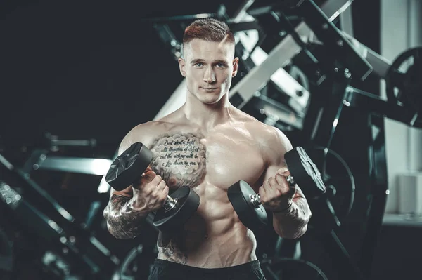 Guapo modelo joven entrenamiento brazos en el gimnasio — Foto de Stock