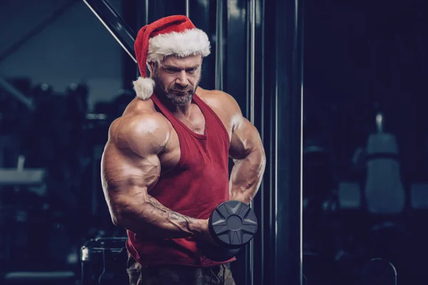 Kulturysta w stroju Świętego Mikołaja na siłowni — Zdjęcie stockowe