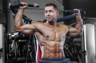 Bodybuilder handsome strong athletic rough man pumping up shoulder muscles workout fitness and bodybuilding healthy concept background - muscular fitness men doing delts exercises in gym naked torso