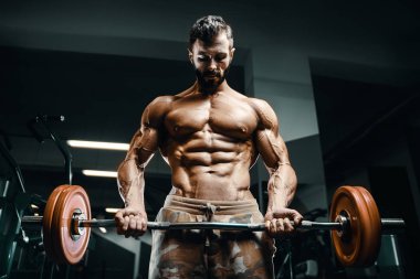 Vücut geliştirici yakışıklı güçlü atletik sert adam kaslarını şişiriyor kaslarını çalıştırıyor sağlıklı bir vücut geliştirme konsepti geliştiriyor kaslı fitness adamları spor salonunda çıplak bedende kol egzersizleri yapıyor.