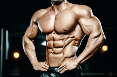 Vücut geliştirici yakışıklı güçlü atletik sert adam karın kaslarını şişiriyor kasları çalıştırıyor vücut geliştirme ve sağlıklı bir konsept geliştirme geçmişi var - kaslı fitness adamları spor salonunda çıplak gövde egzersizleri yapıyor.