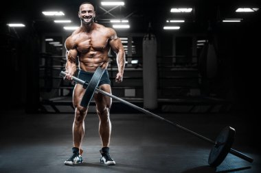 Vücut geliştirici yakışıklı güçlü atletik sert adam karın kaslarını şişiriyor kasları çalıştırıyor vücut geliştirme ve sağlıklı bir konsept geliştirme geçmişi var - kaslı fitness adamları spor salonunda çıplak gövde egzersizleri yapıyor.