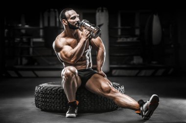 Vücut geliştirici güçlü atletik sert adam egzersiz yaptıktan sonra protein tozuyla vücut geliştirme ve sağlıklı konsept arka planı - kaslı fitness adamları spor salonunda çıplak gövde egzersizleri yapıyor.