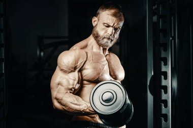 Vücut geliştirici yakışıklı güçlü atletik sert adam kaslarını şişiriyor kaslarını çalıştırıyor sağlıklı bir vücut geliştirme konsepti geliştiriyor kaslı fitness adamları spor salonunda çıplak bedende kol egzersizleri yapıyor.