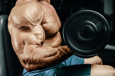 Vücut geliştirici yakışıklı güçlü atletik sert adam kaslarını şişiriyor kaslarını çalıştırıyor sağlıklı bir vücut geliştirme konsepti geliştiriyor kaslı fitness adamları spor salonunda çıplak bedende kol egzersizleri yapıyor.