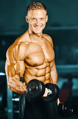 Vücut geliştirici yakışıklı güçlü atletik sert adam kaslarını şişiriyor kaslarını çalıştırıyor sağlıklı bir vücut geliştirme konsepti geliştiriyor kaslı fitness adamları spor salonunda çıplak bedende kol egzersizleri yapıyor.