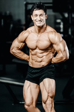 Vücut geliştirici yakışıklı güçlü atletik sert adam karın kaslarını şişiriyor kasları çalıştırıyor vücut geliştirme ve sağlıklı bir konsept geliştirme geçmişi var - kaslı fitness adamları spor salonunda çıplak gövde egzersizleri yapıyor.