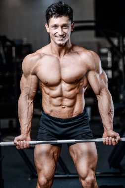Vücut geliştirici yakışıklı güçlü atletik sert adam kaslarını şişiriyor kaslarını çalıştırıyor sağlıklı bir vücut geliştirme konsepti geliştiriyor kaslı fitness adamları spor salonunda çıplak bedende kol egzersizleri yapıyor.