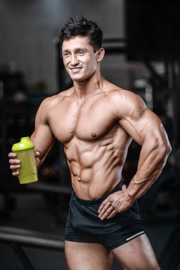Vücut geliştirici güçlü atletik sert adam egzersiz yaptıktan sonra protein tozuyla vücut geliştirme ve sağlıklı konsept arka planı - kaslı fitness adamları spor salonunda çıplak gövde egzersizleri yapıyor.