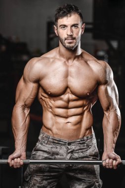 Vücut geliştirici yakışıklı güçlü atletik sert adam kaslarını şişiriyor kaslarını çalıştırıyor sağlıklı bir vücut geliştirme konsepti geliştiriyor kaslı fitness adamları spor salonunda çıplak bedende kol egzersizleri yapıyor.
