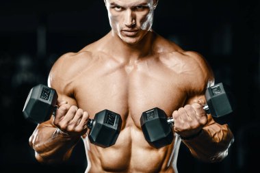 Vücut geliştirici yakışıklı güçlü atletik sert adam kaslarını şişiriyor kaslarını çalıştırıyor sağlıklı bir vücut geliştirme konsepti geliştiriyor kaslı fitness adamları spor salonunda çıplak bedende kol egzersizleri yapıyor.