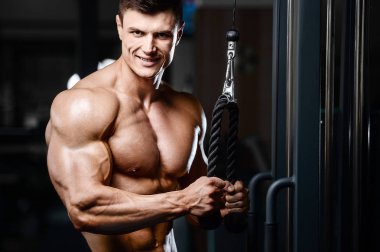 Vücut geliştirici yakışıklı güçlü atletik sert adam kaslarını şişiriyor kaslarını çalıştırıyor sağlıklı bir vücut geliştirme konsepti geliştiriyor kaslı fitness adamları spor salonunda çıplak bedende kol egzersizleri yapıyor.