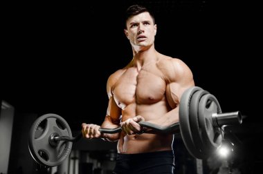 Vücut geliştirici yakışıklı güçlü atletik sert adam kaslarını şişiriyor kaslarını çalıştırıyor sağlıklı bir vücut geliştirme konsepti geliştiriyor kaslı fitness adamları spor salonunda çıplak bedende kol egzersizleri yapıyor.