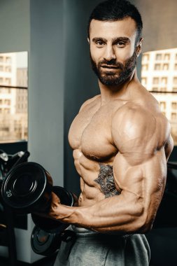 Vücut geliştirici yakışıklı güçlü atletik sert adam kaslarını şişiriyor kaslarını çalıştırıyor sağlıklı bir vücut geliştirme konsepti geliştiriyor kaslı fitness adamları spor salonunda çıplak bedende kol egzersizleri yapıyor.