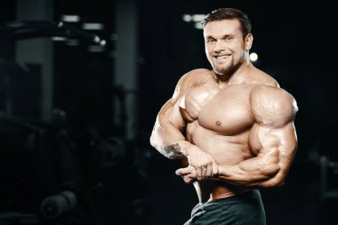 Vücut geliştirici yakışıklı güçlü atletik sert adam kaslarını şişiriyor kaslarını çalıştırıyor sağlıklı bir vücut geliştirme konsepti geliştiriyor kaslı fitness adamları spor salonunda çıplak bedende kol egzersizleri yapıyor.
