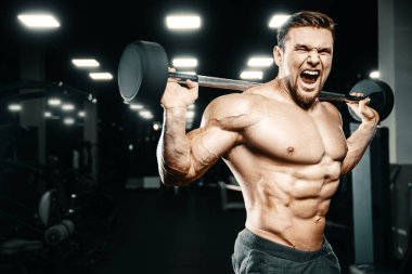 Vücut geliştirici yakışıklı güçlü atletik sert adam karın kaslarını şişiriyor kasları çalıştırıyor vücut geliştirme ve sağlıklı bir konsept geliştirme geçmişi var - kaslı fitness adamları spor salonunda çıplak gövde egzersizleri yapıyor.