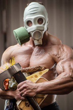 Baltalı vücut geliştirici sporcu, spor salonunda gaz maskeli yemek. Peynirli yumurta ve mısır gevreğiyle kaslı adam Coronavirüs salgını covid-19 pandemik kaos medikal maske kıyamet sonrası vücut geliştirme.