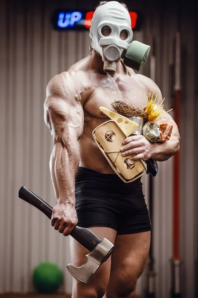 Bodybuilder athlete with axe, food in gas mask in gym. Muscle man with cheese eggs and cereals coronavirus epidemic covid-19 pandemic chaos medical mask post-apocalypse fitness delivery bodybuilding