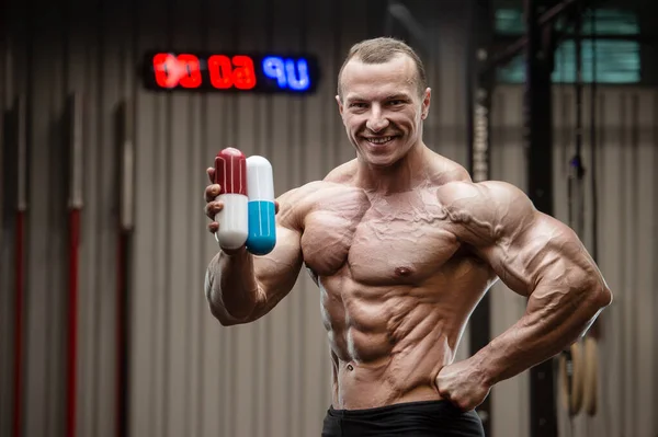 Fitness man in medical mask. Muscle man in gym with pill, tablet, ampoule drugs, virus concept. Coronavirus disease COVID-19 infection. Caucasian bodybuilder with steroids, bodybuilding gym exercises