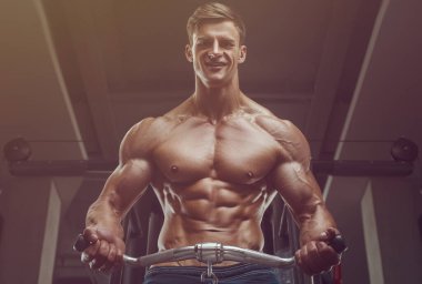Vücut geliştirici yakışıklı güçlü atletik sert adam kaslarını şişiriyor kaslarını çalıştırıyor vücut geliştiriyor sağlıklı bir konsept geliştiriyor kaslı fitness adamları spor salonunda çıplak bedende kol egzersizleri yapıyor.