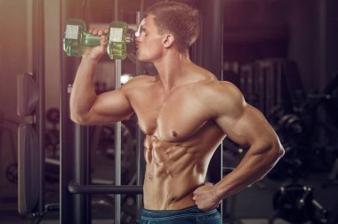 Vücut geliştirici güçlü atletik sert adam vücut geliştirme egzersizi ve vücut geliştirme konsepti tasarımından sonra su içiyor. Kas geliştiren sporcular spor salonunda çıplak gövde egzersizleri yapıyor.