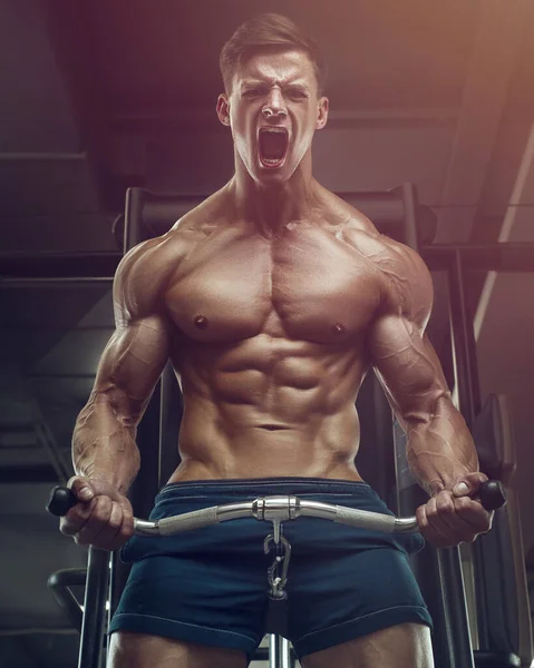 Vücut geliştirici yakışıklı güçlü atletik sert adam kaslarını şişiriyor kaslarını çalıştırıyor vücut geliştiriyor sağlıklı bir konsept geliştiriyor kaslı fitness adamları spor salonunda çıplak bedende kol egzersizleri yapıyor.