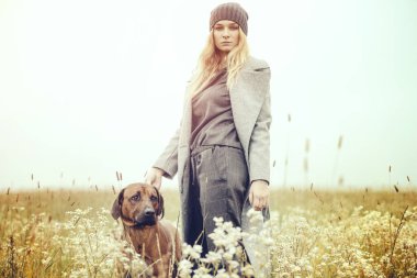 Güzel, hoş, hoş, güzel, beyaz, sarışın, genç, moda elbiseli, açık havada köpekli kız kırsal alanda bahar veya sonbahar havası depresif.