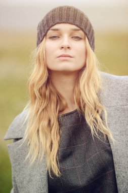 Güzel giyimli, güzel, beyaz, sarı saçlı, şık elbiseli, genç bir kız. Paltolu, açık hava, çiftlik evinin yanında, kırsal alanda, bahar veya sonbahar havası depresif.