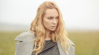 Güzel giyimli, güzel, beyaz, sarı saçlı, şık elbiseli, genç bir kız. Paltolu, açık hava, çiftlik evinin yanında, kırsal alanda, bahar veya sonbahar havası depresif.