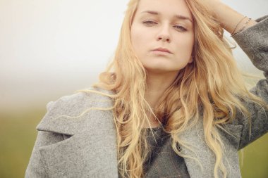 Güzel giyimli, güzel, beyaz, sarı saçlı, şık elbiseli, genç bir kız. Paltolu, açık hava, çiftlik evinin yanında, kırsal alanda, bahar veya sonbahar havası depresif.