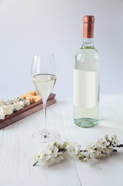 Bir şişe şarap, peynir ve çiçekler ahşap bir arka planda