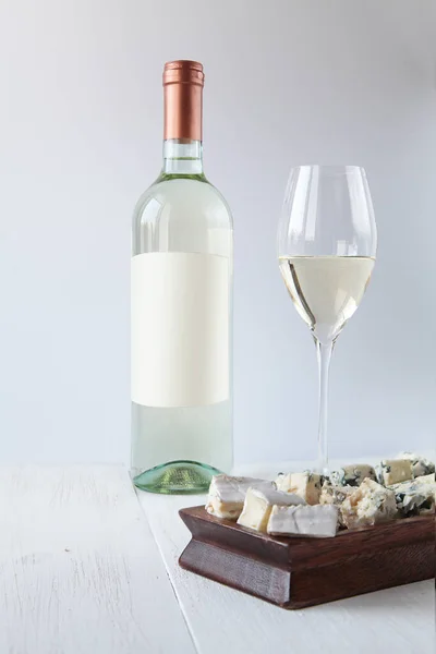 Bir şişe beyaz şarap, tahtanın üzerinde bir bardak ve peynir.