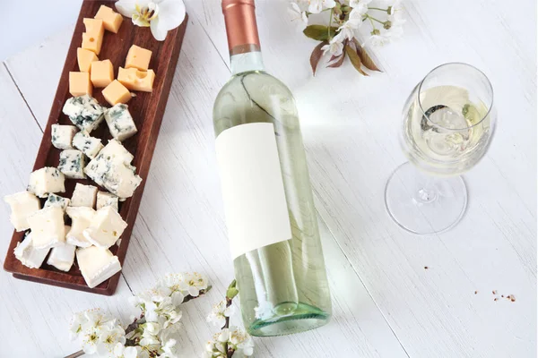 Bir şişe şarap, şarap bardakları, peynir ve çiçekler ahşap arka planda.