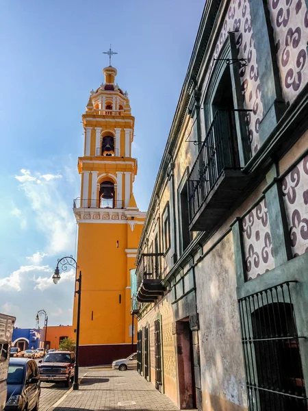 Bright yellow facade of the San Apostolo church in the Zocalo in Cholula, Mexico viewed across lawns and shrubs against a blue sky — Stock Photo, Image