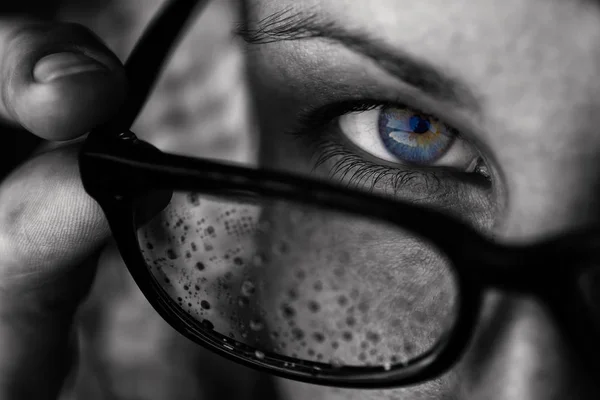 青い目の少女は彼女のメガネに見えます メガネは 滴の水 で覆われています 目に重点を置いて 黒と白のイメージ — ストック写真