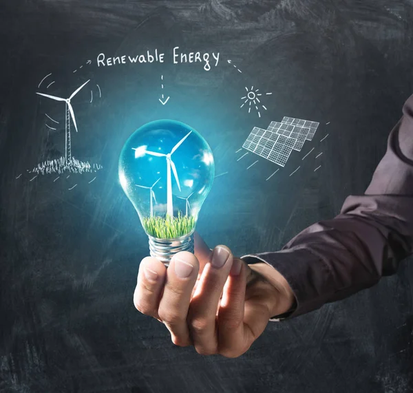 可再生能源概念 手中握有一个灯泡长满绿草和风车里面黑板背景 — 图库照片