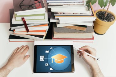 Tablet, kalem, kitaplar, cam, saksı ve erkek eli masanın üstünde. Farklı eğitim simgelerine sahip tablet (mezuniyet şapkası, sertifika, kitap, dizüstü bilgisayar, diyalog, büyüteç, grafik). E-öğrenim kavramı, çevrimiçi kurs, giyim.