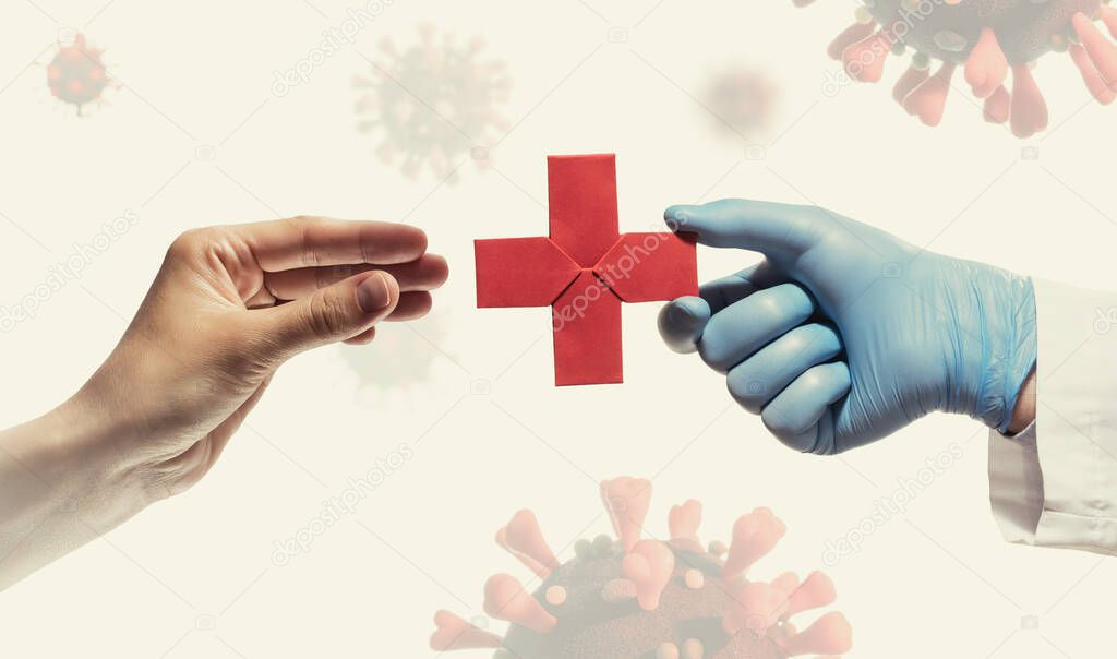Doctor's hand gives a red paper cross  to a woman. Image on background with coronavirus covid-19. Concept of medical treatment during the pandemic covid-19