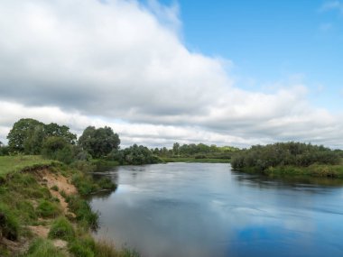 Bulutlar bir nehrin pürüzsüz sularında yansıyor..