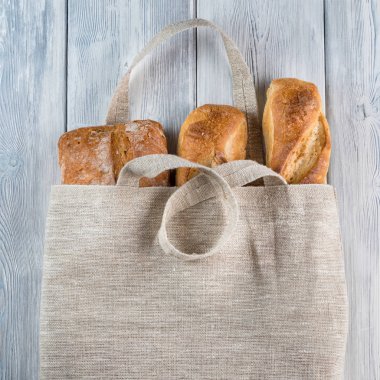 Ekmeğin yeniden kullanılabilir sıfır atık tekstil torbasında beyaz ahşap zemin üzerinde üst görünümü.