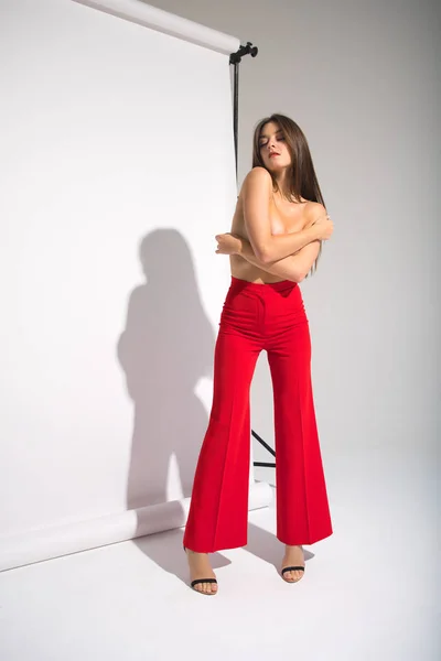 Schöne nackte Frau in roten Hosen posiert Schatten werfen isoliert auf dem grauen Hintergrund — Stockfoto