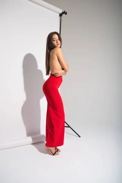 Schöne nackte Frau in roten Hosen posiert Schatten werfen isoliert auf dem grauen Hintergrund — Stockfoto