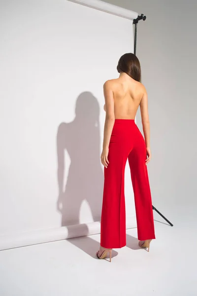 Mooie naakte vrouw In rode broek poseren werpt schaduw geïsoleerd op de grijze achtergrond — Stockfoto