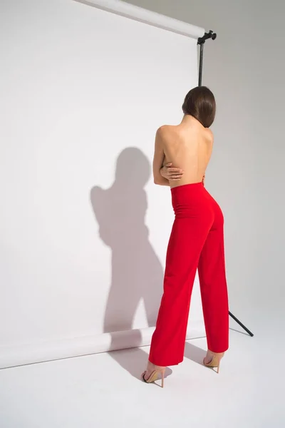 Beautiful Naked Woman In Red Pants Posing Casting Shadow Isolated On The Gray Background