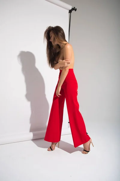 Красивая голая женщина в красных штанах, позирующая отбрасывающая тень, изолированная на сером фоне — стоковое фото