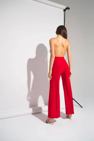 Vacker naken kvinna i röda byxor poserar kastar skugga isolerat på den grå bakgrunden Stockfoto